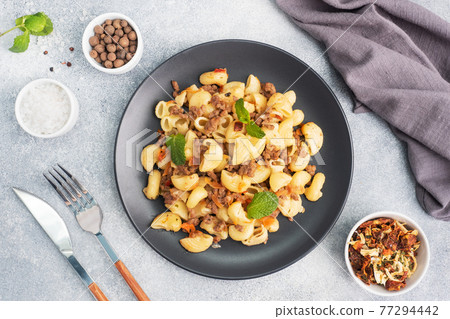 Stewed pasta with minced beef and vegetables, macaroni in Navy style on a plate. grey concrete background. Stewed pasta with minced beef and vegetables, macaroni in Navy style on a plate. grey concrete background. 77294442
