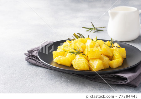 Delicious baked potatoes with spices cheese and rosemary on a black ceramic plate, a gray concrete background, copy space. Delicious baked potatoes with spices cheese and rosemary on a black ceramic plate, a gray concrete background, copy space. 77294443
