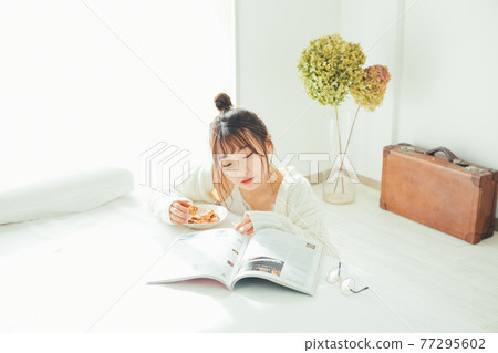 一個女孩一邊吃零食一邊看雜誌 一個女孩一邊吃零食一邊看雜誌 77295602