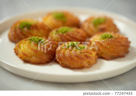 Turkish and Arabic Traditional Ramadan Dessert Lor Cheese Dessert with pistachio powder and syrup serving on plate. 77297485