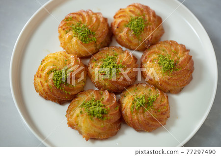 Turkish and Arabic Traditional Ramadan Dessert Lor Cheese Dessert with pistachio powder and syrup serving on plate. 77297490