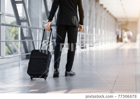 Cropped of businessman walking by airport with suitcase, back view Cropped of businessman walking by airport with suitcase, back view 77306878
