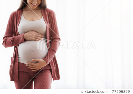 Closeup Shot Of Young Woman Embracing Her Pregnant Belly And Smiling 77306899