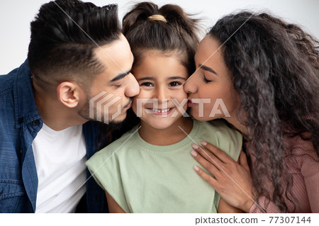 Happy Family Portrait. Closeup Shot Of Loving Arab Parents Kissing Little Daughter Happy Family Portrait. Closeup Shot Of Loving Arab Parents Kissing Little Daughter 77307144