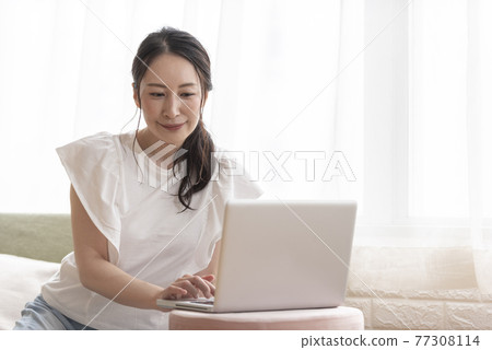A woman operating a computer while sitting at home A woman operating a computer while sitting at home 77308114
