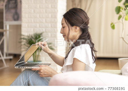 A woman operating a computer while sitting at home A woman operating a computer while sitting at home 77308191