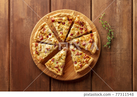 A photo of a quiche with thyme, shot from the top on a dark rustic wooden background A photo of a quiche with thyme, shot from the top on a dark rustic wooden background 77311548