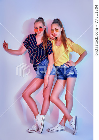 Two female teenagers in sunglasses and summer clothes posing in studio on white background 77311804