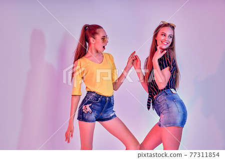 Two female teenagers in sunglasses and summer clothes posing in studio on white background Two female teenagers in sunglasses and summer clothes posing in studio on white background 77311854