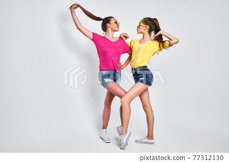Two young beautiful smiling international hipster female in trendy summer clothes. Sexy carefree women posing on white background in studio. Two young beautiful smiling international hipster female in trendy summer clothes. Sexy carefree women posing on white background in studio. 77312130