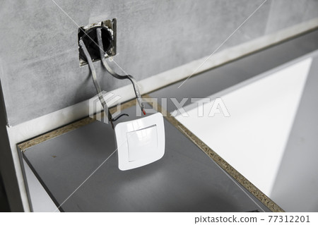 Repair or installation of a new light switch in the wall. Light switch connected via cables to a electricity in a home. 77312201