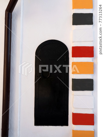 Beautiful fragment of white church with colorful ornament and black iron wrought door background. 77313264