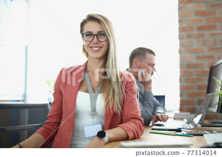 Young smiling businesswoman sits at working table on background of business office Young smiling businesswoman sits at working table on background of business office 77314014