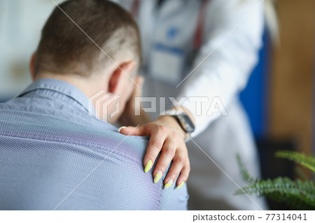 Doctor put her hand sympathetically on shoulder of upset male patient 77314041