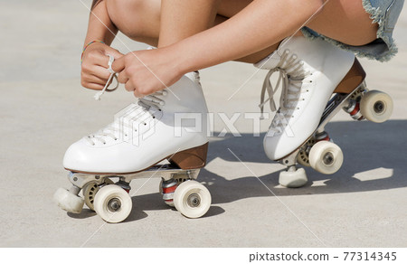 Close-up detail of skater's hands tying the laces of a roller skate 77314345