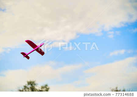 A pink plastic children's airplane toy flying in blue sky surrounded with white clouds A pink plastic children's airplane toy flying in blue sky surrounded with white clouds 77314688