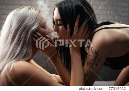two young women inhale smoke on each other's lips while kissing showing the closeness of an LGBT relationship two young women inhale smoke on each other's lips while kissing showing the closeness of an LGBT relationship 77316012