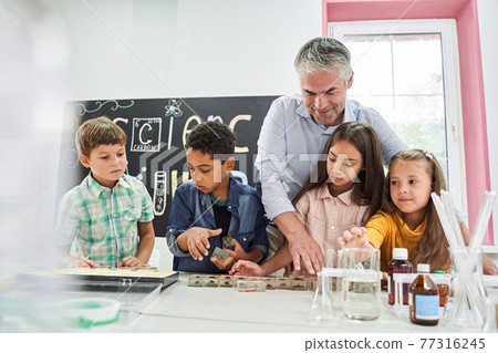 Teacher laying out insect samples in glass in front of restless childrens Teacher laying out insect samples in glass in front of restless childrens 77316245
