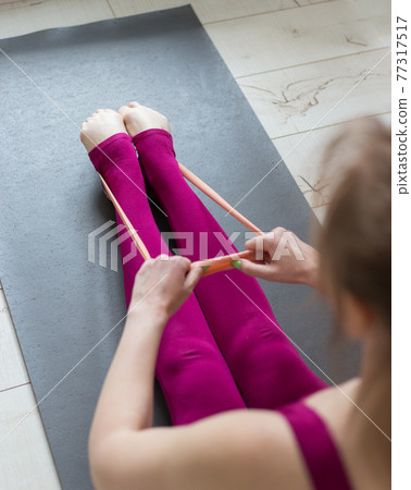 Resistance band exercise at home. Woman doing pilates workout using elastic strap pulling with arms for shoulder training on yoga mat indoors. Sport and healthy active lifestyle concept. Resistance band exercise at home. Woman doing pilates workout using elastic strap pulling with arms for shoulder training on yoga mat indoors. Sport and healthy active lifestyle concept. 77317517