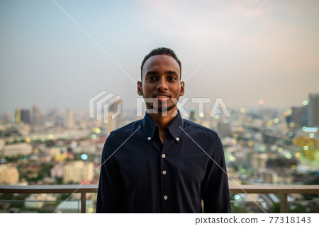 Portrait of handsome African businessman outdoors at rooftop smiling 77318143