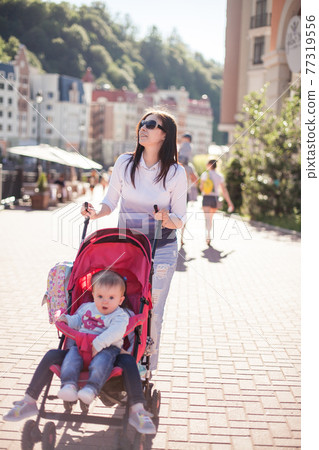 young mother walking with baby in stroller young mother walking with baby in stroller 77319556