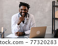 Handsome contented African American doctor working on a laptop. telemedicine 77320283
