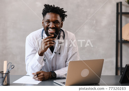 Handsome contented African American doctor working on a laptop. telemedicine 77320283