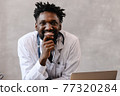 Handsome contented African American doctor working on a laptop. telemedicine 77320284