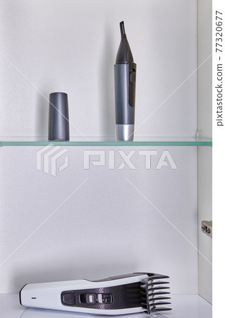 Household appliances for home haircuts such as nose, eyebrow and ear trimmer and head hair clipper are stored in bathroom wall cabinet. Household appliances for home haircuts such as nose, eyebrow and ear trimmer and head hair clipper are stored in bathroom wall cabinet. 77320677