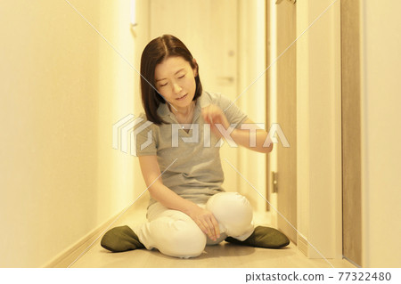 Tired, middle-aged woman sitting in the hallway Tired, middle-aged woman sitting in the hallway 77322480