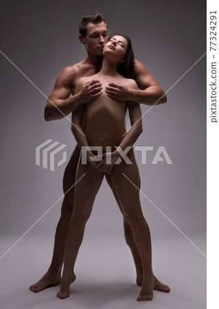 Naked couple standing in studio - man cover woman breast Naked couple standing in studio - man cover woman breast 77324291