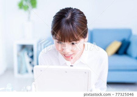 一位年輕女子在客廳裡照鏡子時塗口紅 一位年輕女子在客廳裡照鏡子時塗口紅 77325046