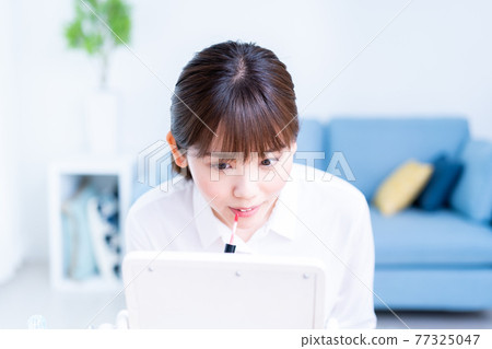 一位年輕女子在客廳裡照鏡子時塗口紅 一位年輕女子在客廳裡照鏡子時塗口紅 77325047