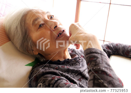 一位老婦人躺在護理床上，思考著她的下巴 77325953