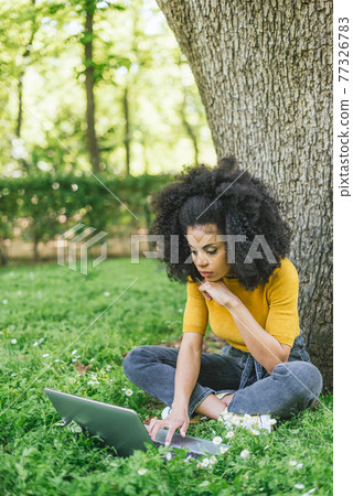 Beautiful afro woman typing on a laptop in a garden. 77326783