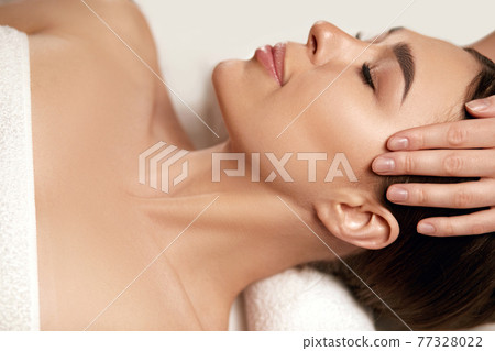 Face massage. Beautiful of young woman getting spa massage treatment at beauty spa salon.Spa skin and body care. Facial beauty treatment.Cosmetology. 77328022