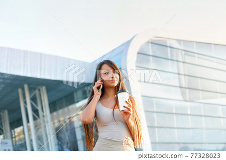 Happy Woman Calling On Phone Standing Near Office. Portrait Of Beautiful Smiling Female Holding Cup Of Coffee In Hand, Talking On Phone Outdoors. 77328023
