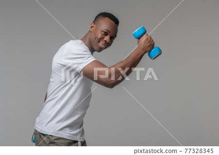 Attractive joyful man with dumbbells doing sports 77328345