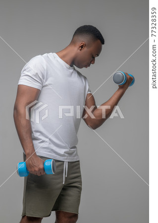 Muscular darkskinned man doing exercises with dumbbells Muscular darkskinned man doing exercises with dumbbells 77328359