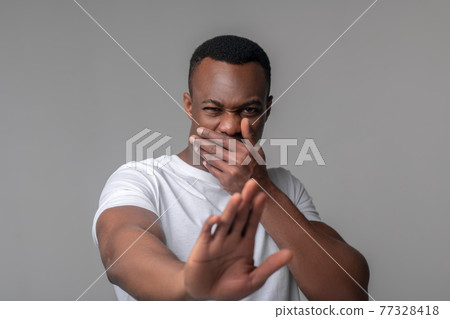 Man with grimace covering mouth with hand Man with grimace covering mouth with hand 77328418