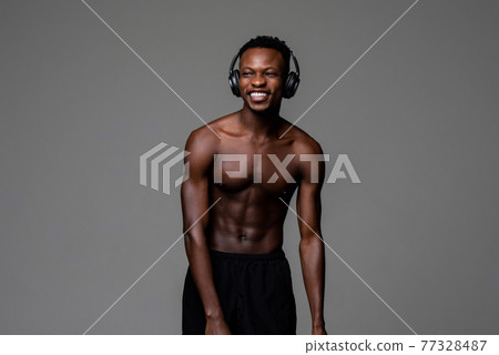 Shirtless fit happy young African man wearing headphones and smiling Shirtless fit happy young African man wearing headphones and smiling 77328487