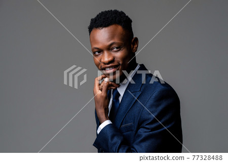 Smiling young handsome African man wearing formal business suit thinking with hand touching face 77328488