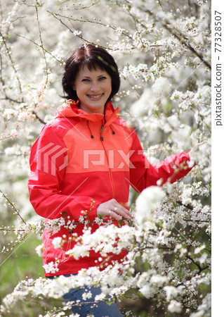 Beautiful mature woman posing for the camera in a blooming spring garden. 77328507