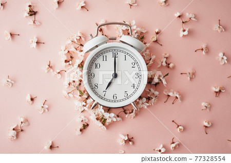 Alarm clock on pink background with flowers. Change time concept 77328554