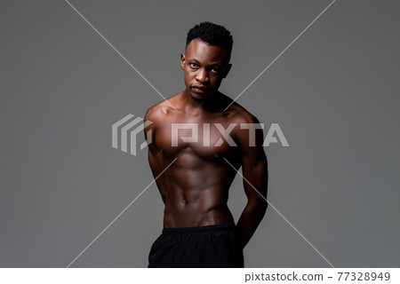 Studio shot of handsome shirtless lean fit African man lookig at camera in isolated gray background 77328949