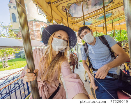 Man and woman wearing a medical mask during COVID-19 coronavirus at an amusement park 77329049
