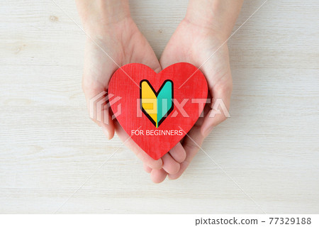 Female hand holding a heart-shaped object with a beginner mark 77329188