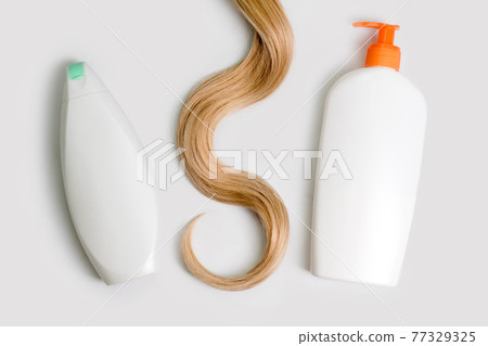 Shampoo and conditioner bottles and lock of curly blonde hair isolated on light background, top view. Flat lay, copy space for text. Hair care cosmetics, beauty haircare products, hair treatment. 77329325