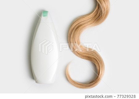 Shampoo or conditioner bottle and lock of curly blonde hair isolated on light background, top view. Flat lay, copy space for text. Hair care cosmetics, beauty haircare products, hair treatment. 77329328