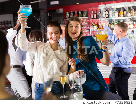 Two smiling girls drinking cocktails Two smiling girls drinking cocktails 77329821